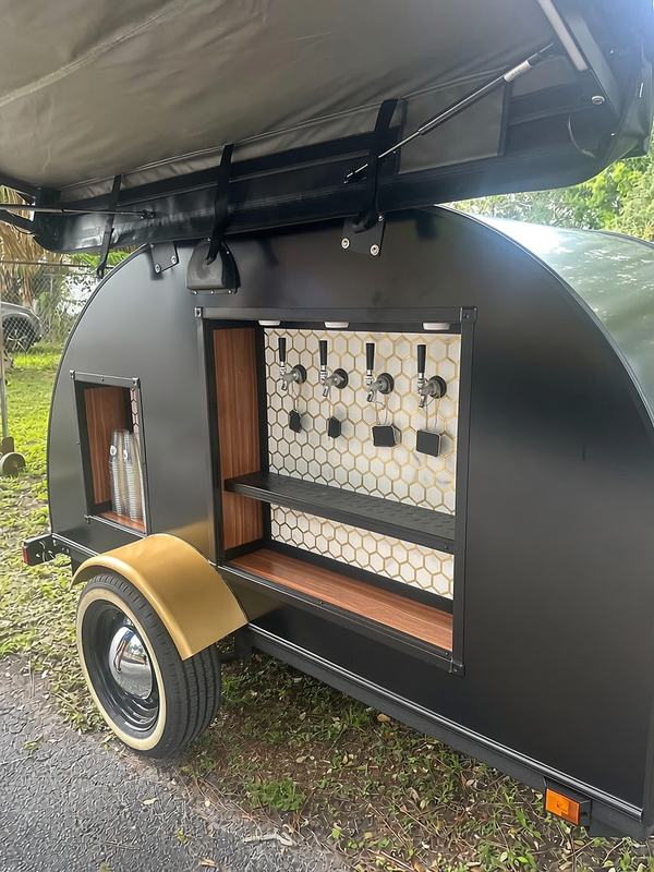 Tap trailer with its awning open, set up on a lawn for an outdoor party